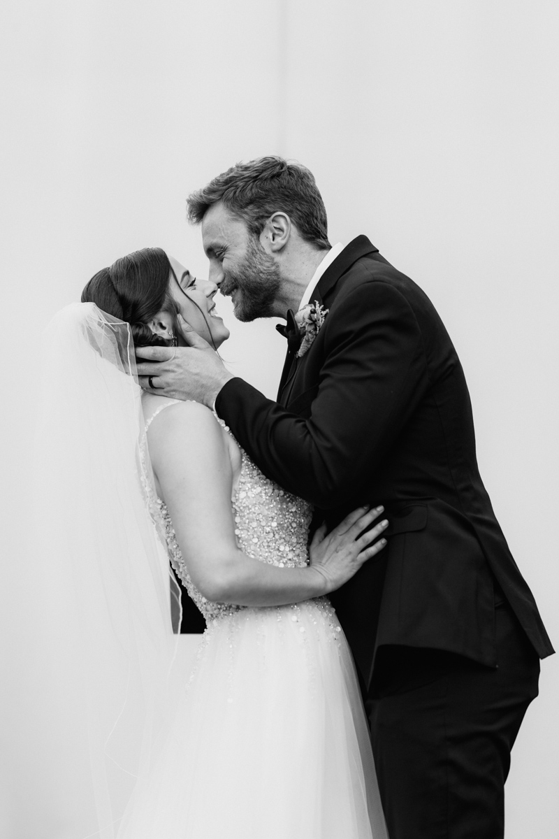 Photo of a Couple in Amherst, Massachusetts. Bride and Groom embracing one another as they have their first kiss with a plain white background behind them