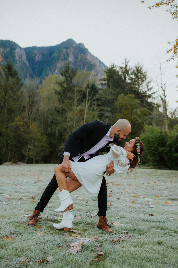 Bride and Groom in a forest location in Washington. Groom wearing a nice, relaxed suit with a pink shirt and blue fabric for pants and jacket, dipping the bride back.
