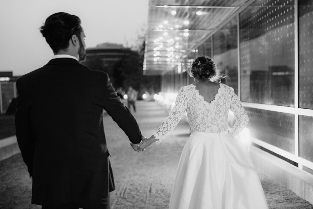 Photo of a Bride and Groom walking in Downtown Seattle at night. The bride is holding her dress in one hand and holding the grooms hand in the other as they walk back to the reception