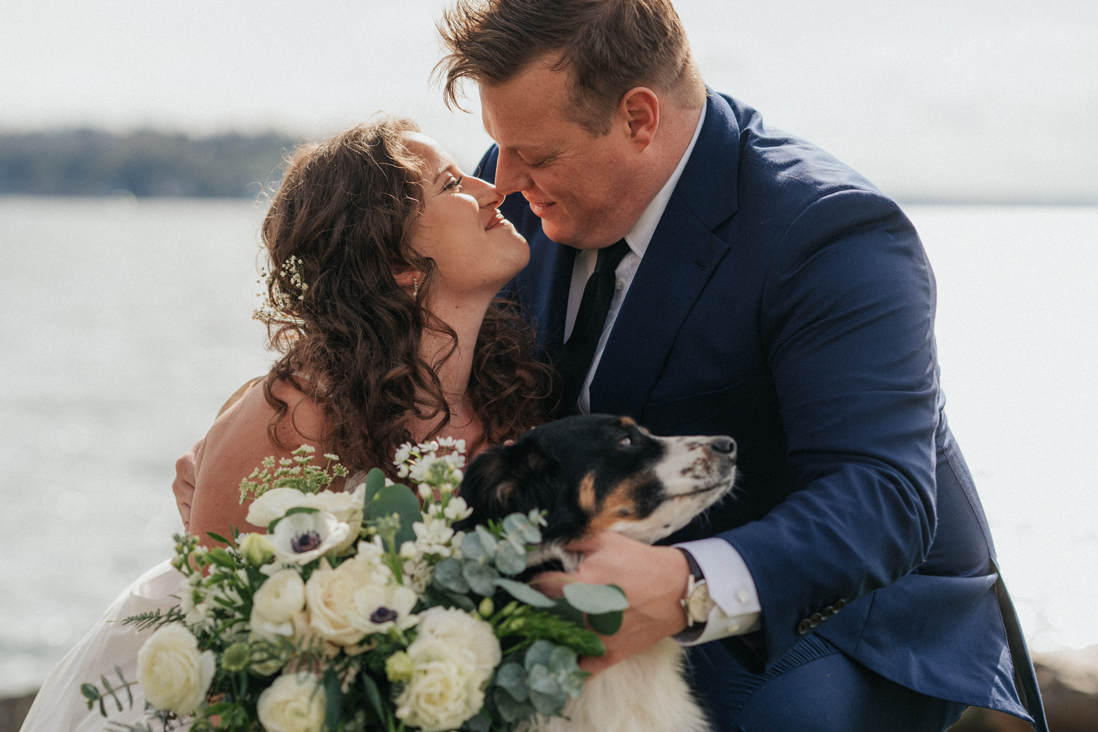 Photo of a couple in Seattle Washington. Couple looking at each other smiling and about to kiss while they hug their dog.