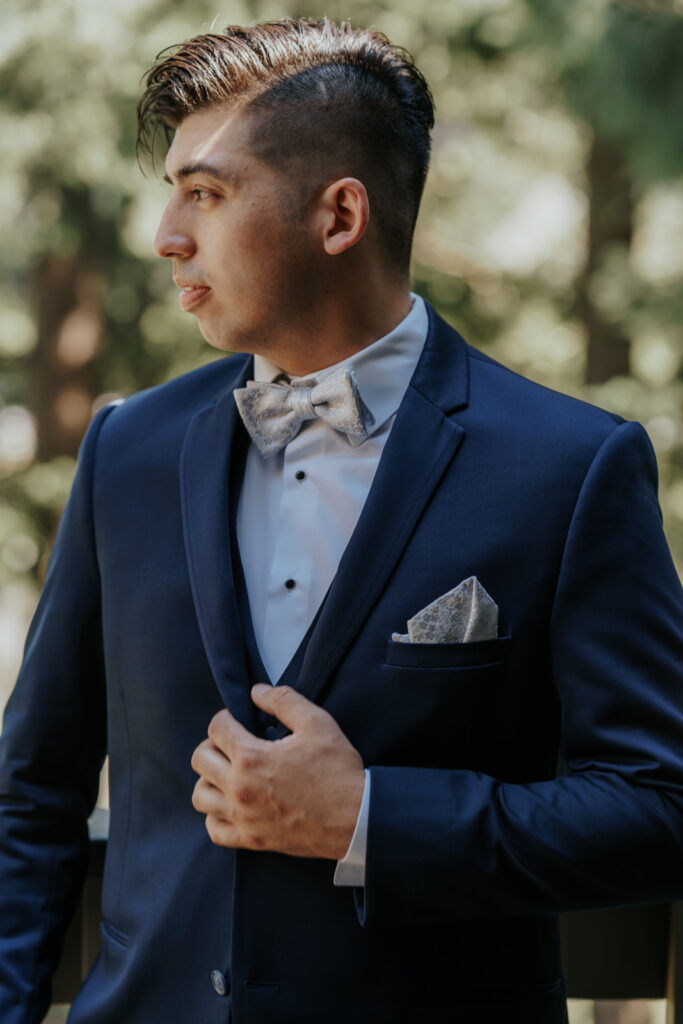 Photo of a Groom in San Juans, checking his three piece suit in a nice blue, with a fun pattern pocket square tucked away and bow tie to match.