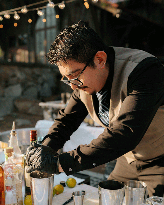 GIF image of a bartender in a well fitting vest and black shirt, making cocktails at a wedding in Washington. He has a great blue patterned tie with an eyeglasses tie holder.