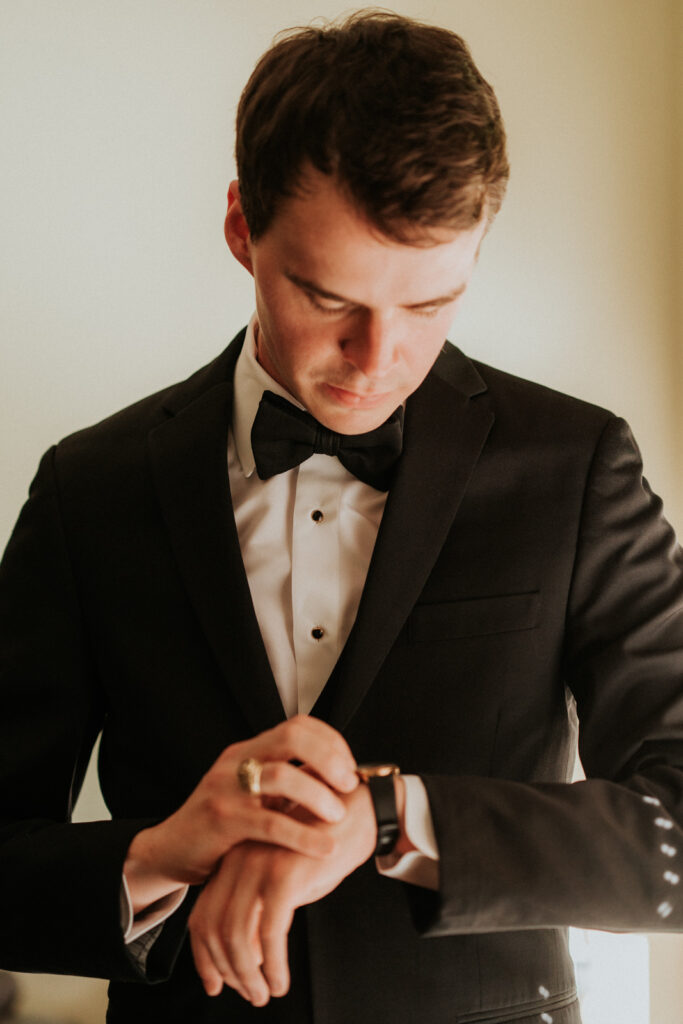 Photo of a Man in Seattle, checking his wristwatch after getting into his custom suit that's all black with black bowtie.